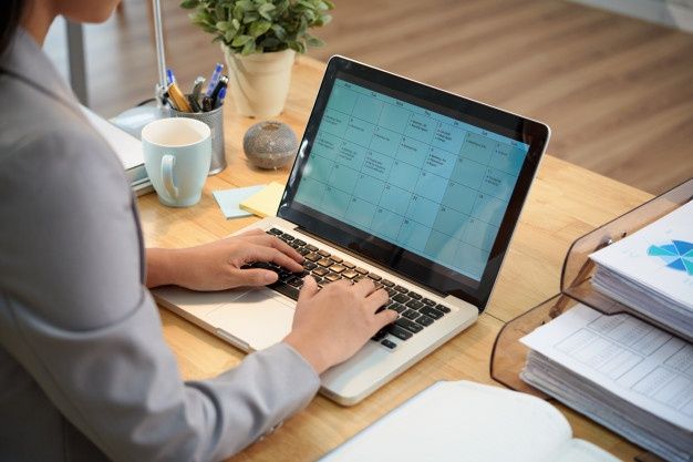 Free Photo Unrecognizable businesswoman sitting at desk with laptop and looking at calendar